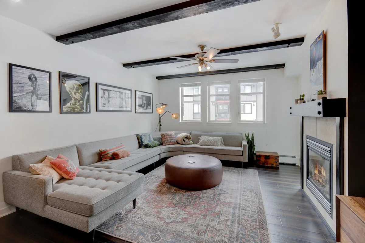 The image showcases a spacious, inviting living area with a plush sectional sofa arranged around a modern round coffee table and a glowing fireplace. Tasteful artwork adorns the walls, creating a warm, stylish atmosphere perfect for gathering with friends and family.