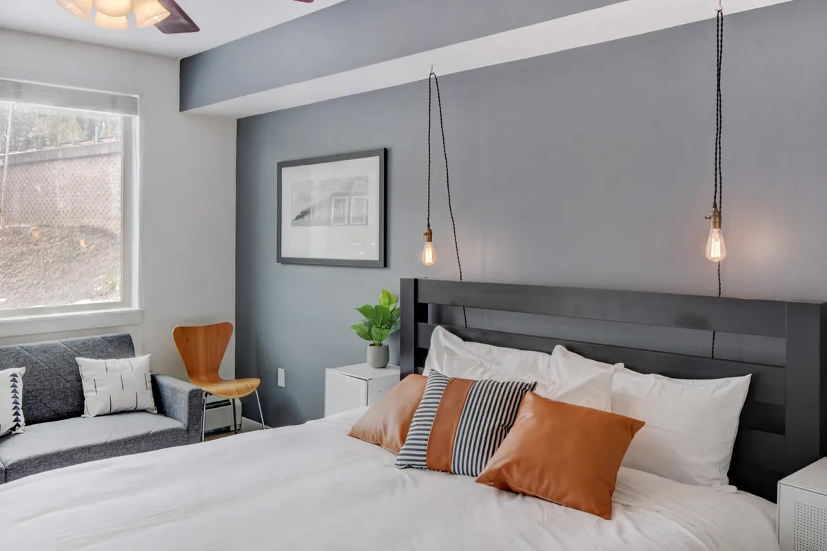 A tranquil bedroom with a large bed adorned with decorative pillows, soft pendant lighting, a cozy sofa and chair, and a window letting in natural light. The space feels both luxurious and inviting, ideal for unwinding after a day of mountain adventures.