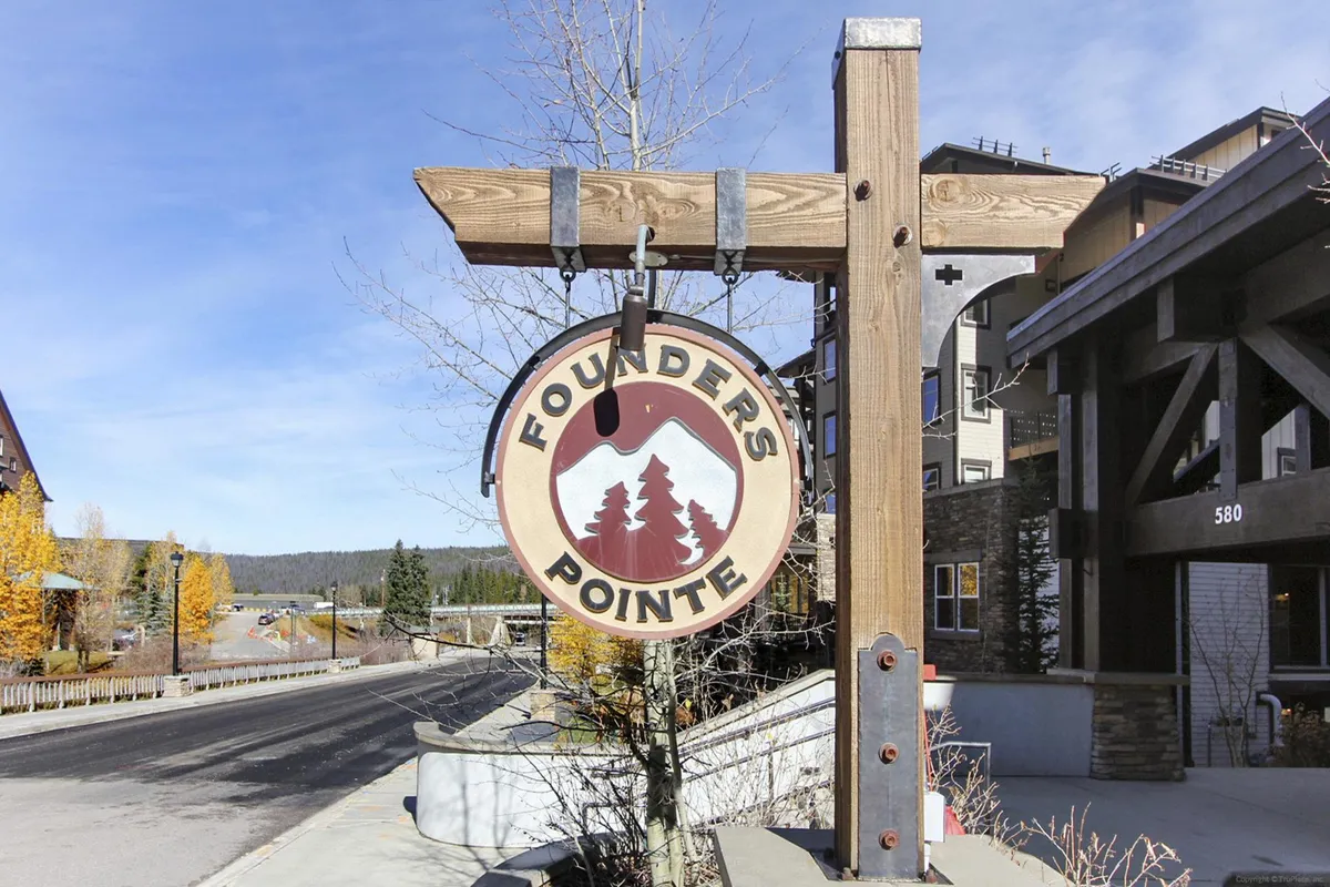 An inviting entrance to the property, marked by the Founder's Pointe sign, surrounded by trees and distinct building architecture. The scene conveys a welcoming atmosphere and hints at the communal and resort-style amenities available to guests.