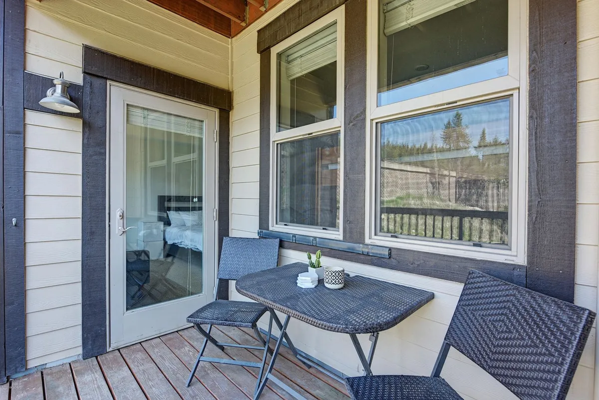 This exterior image captures a cozy outdoor patio featuring a table and chairs set against the backdrop of a doorway and windows. The seating area suggests an ideal spot for enjoying a morning coffee or relaxing with friends, with a relaxed atmosphere enhanced by natural light.