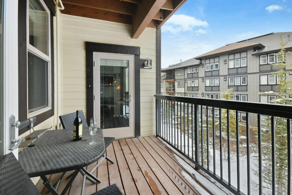 An exterior shot of a covered deck with comfortable seating, a wine bottle, and glassware set out, all overlooking a beautiful mountain sunset. The inviting setup encourages outdoor relaxation and socializing while enjoying the scenic surroundings.