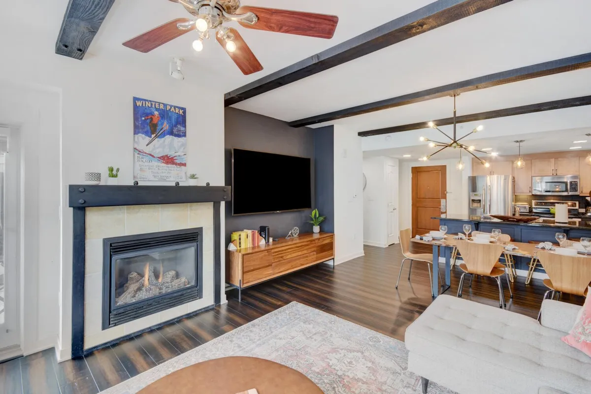 A warm, welcoming interior scene showcasing a dining area adjacent to a kitchen island and a cozy fireplace. The space is accented by artwork on the wall and evokes feelings of togetherness, perfect for relaxing or celebrating with friends and family.
