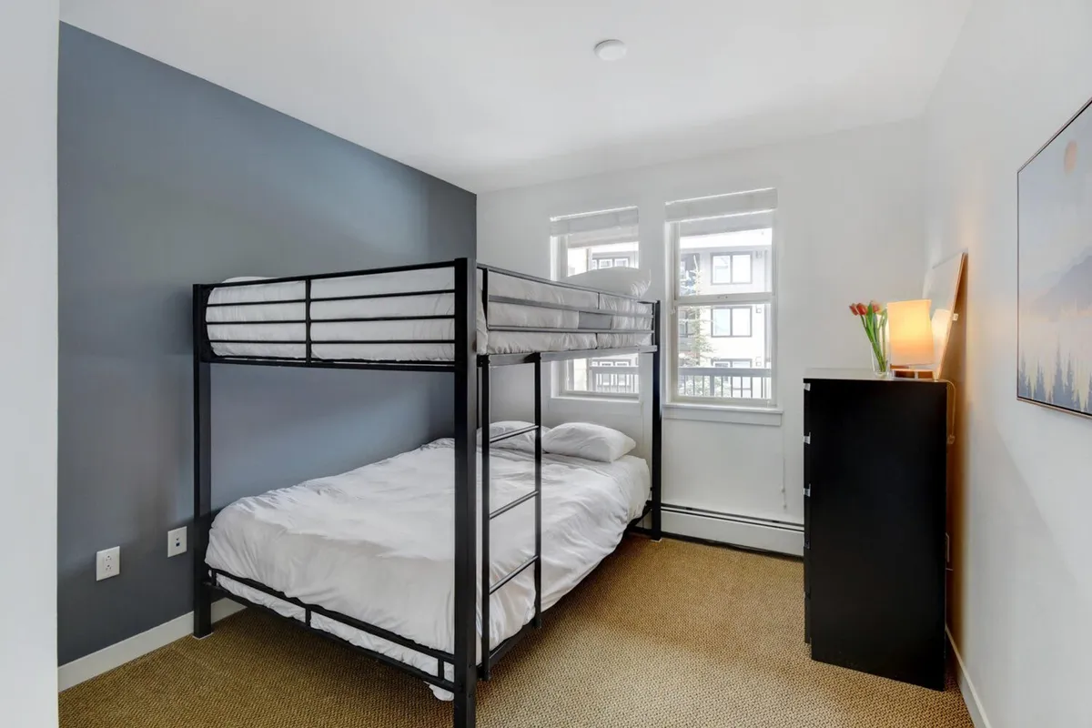 A bright bunk room with a substantial bunk bed, nightstand, and sunlit window. The room feels practical yet welcoming, providing the perfect setup for children, teens, or groups to share stories and enjoy restful nights together.