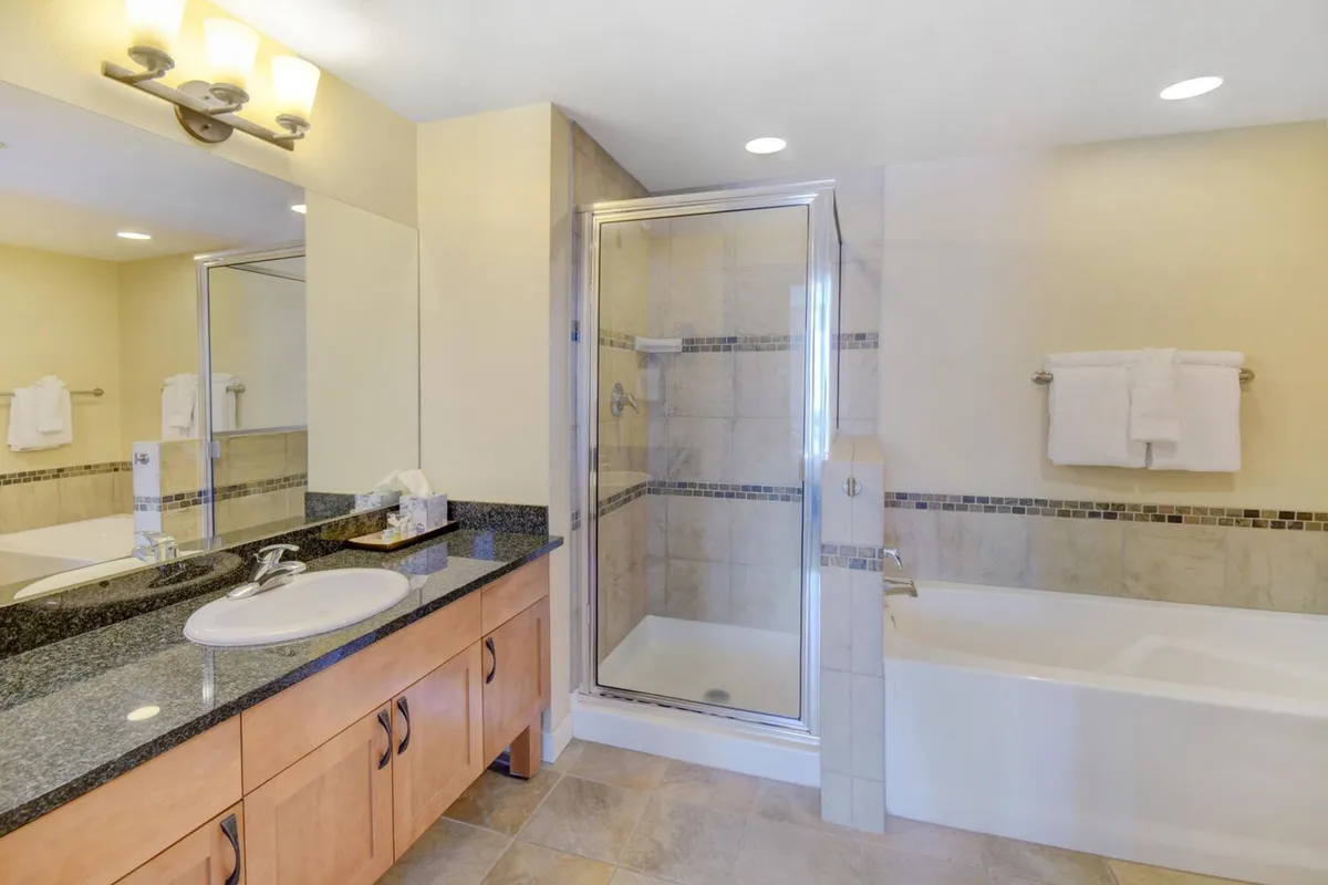 A modern bathroom featuring a sleek vanity with sink, large mirrored wall, glass shower enclosure, and a freestanding bathtub. The overall feel is calm, rejuvenating, and reminiscent of a spa, perfect for unwinding and self-care.
